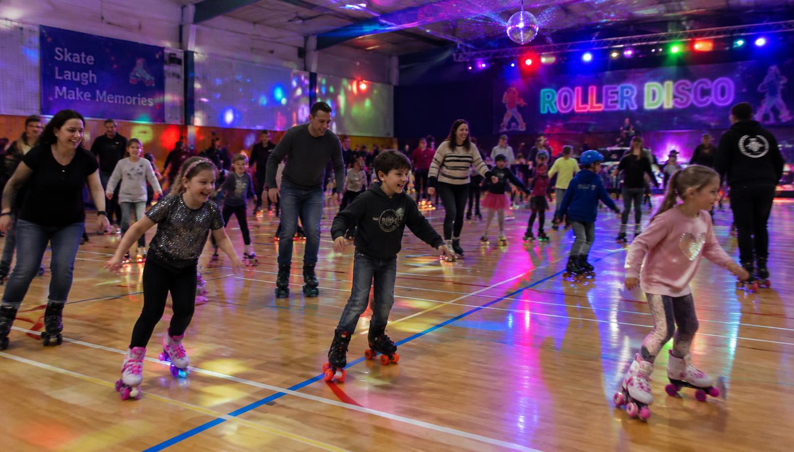 Families roller skating at a disco-lit leisure centre hall